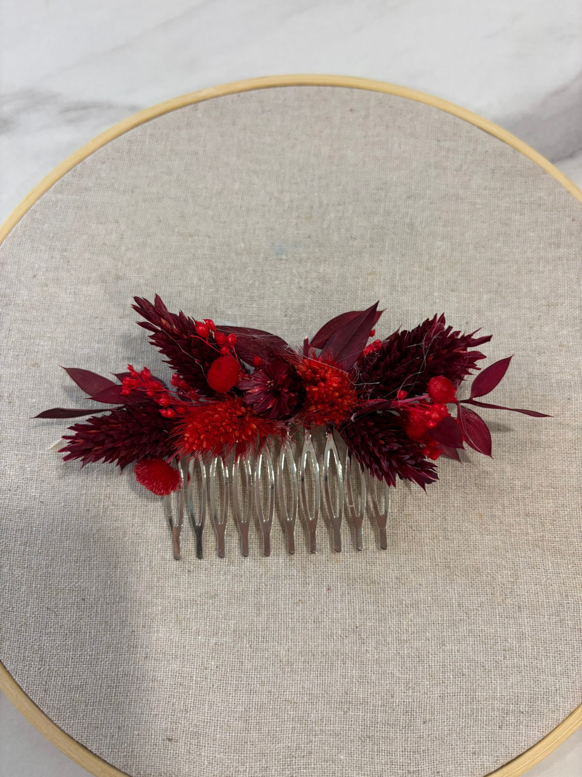 Peigne rouge Rêves En Fleurs en plastique avec dents fines et longues, posé sur une surface claire.